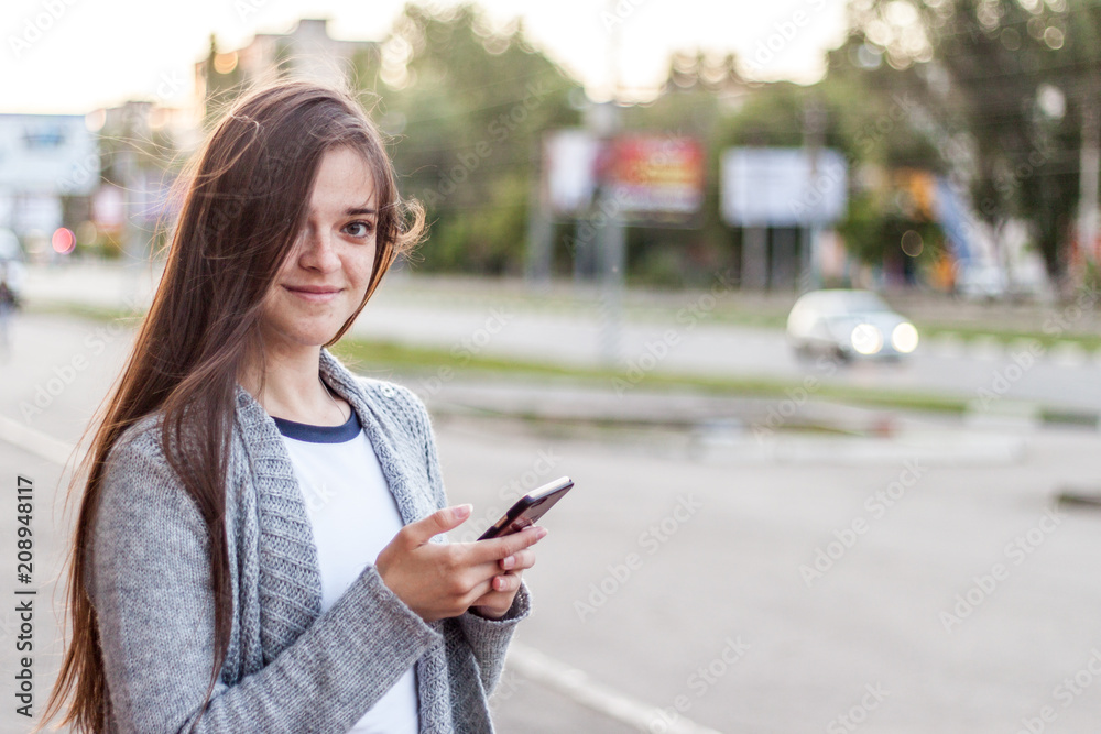 Smiling longhair girl using her smartphone at the city street at summer day Smiling longhair girl using her smartphone at the city street at summer day