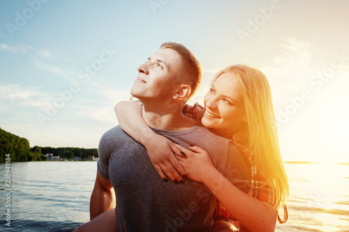 couple happy, girl sits on a guy couple on the beach sunset