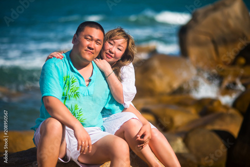 Adult Asian couple sitting on stones on the sea background