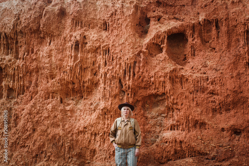 Beautiful young girl in hare, hat and with backpack travels among sands in wild