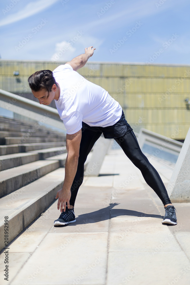 Fototapeta premium Athletic man warming up before running. Workout in the urban city.