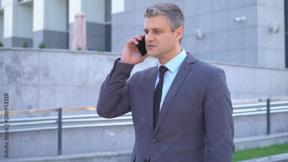 Attractive middle-aged man. cheerful businessman talking on the phone. An image of a general plan, against the background of modern office buildings. A solid gray-haired man in a jacket and tie 4K Attractive middle-aged man. cheerful businessman talking on the phone. An image of a general plan, against the background of modern office buildings. A solid gray-haired man in a jacket and tie 4K