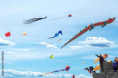 Man is holding huge flying kite in blue cloudy sky