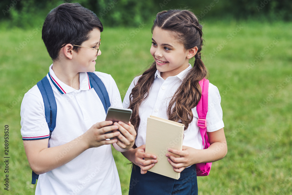 smiling schoolchildren using smartphone outdoors together smiling schoolchildren using smartphone outdoors together