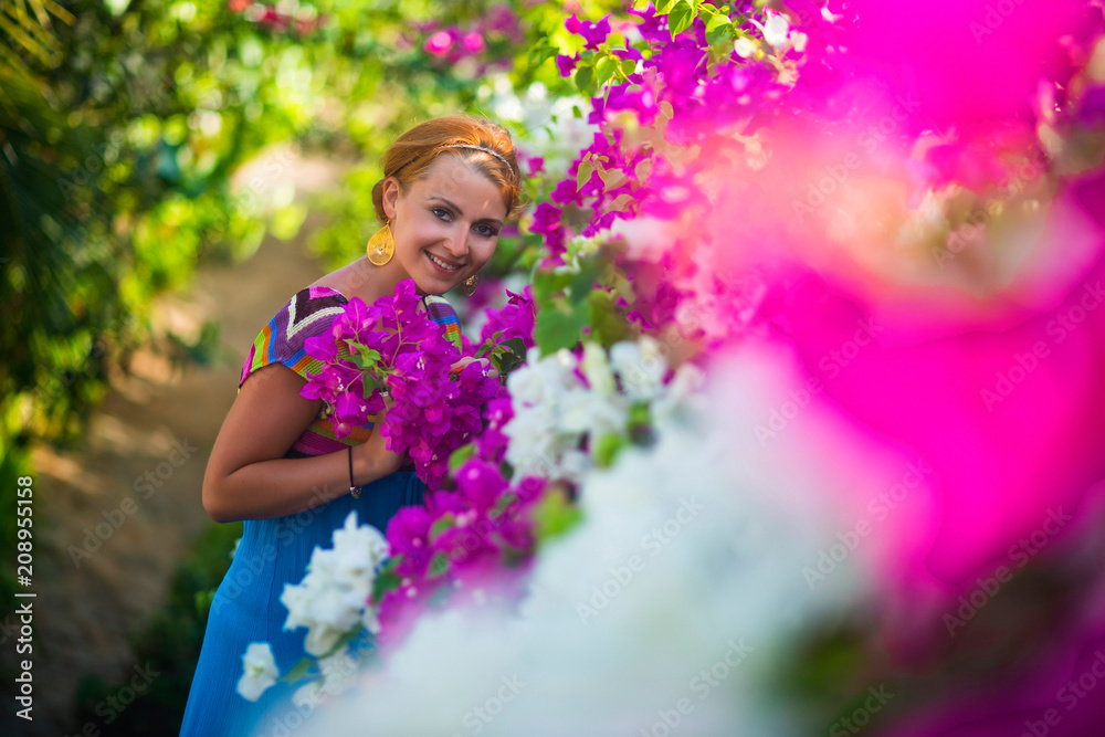 Young beautiful woman standing in the middle of flowers. The girl is dressed in a blue dress, she is surrounded by purple and white flowers. Young beautiful woman standing in the middle of flowers. The girl is dressed in a blue dress, she is surrounded by purple and white flowers.