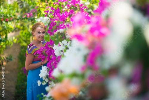 Young beautiful girl posing in a flower garden. The girl is dressed in a blue dress, she is surrounded by purple and white flowers.