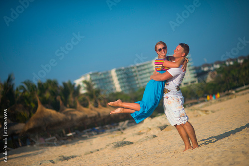Woman jumping into the arms of men on the beach against the palm trees and sky. The sand flies on the sides