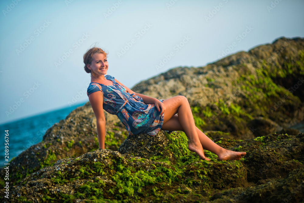 Woman sitting on stones against the ocean at sunset