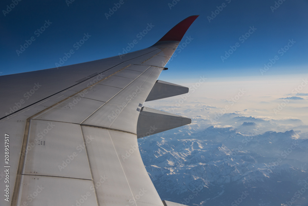 Snow mountain view in Europe with airplane wing through aircraft window