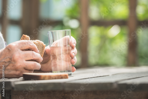 hands of the grandmother hold a glass and bread on a wooden table