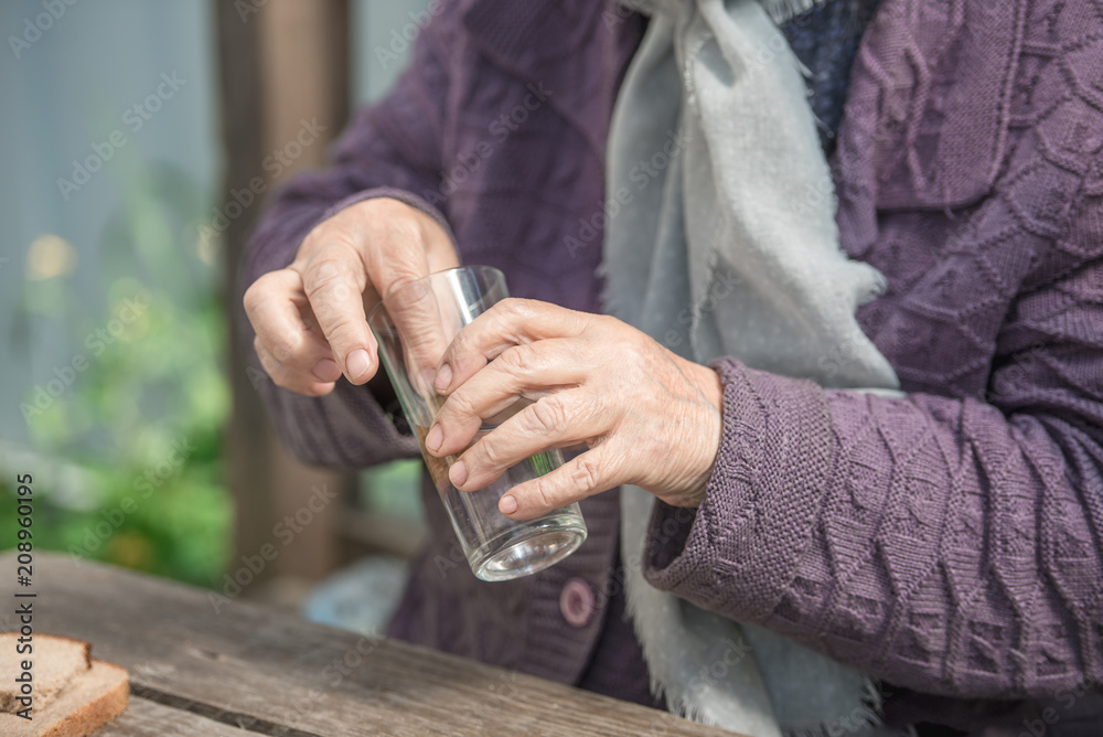 The old woman drinks water and eats bread at an old wooden table in a garden