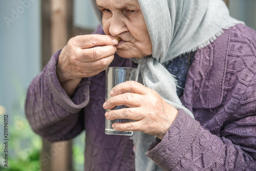 The old woman drinks water and eats bread at an old wooden table in a garden