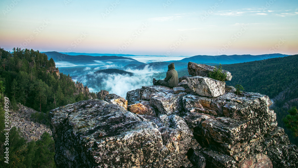 Man traveller sitting on rock at mountain top and meeting sunrise, heavy mist in deep valley.