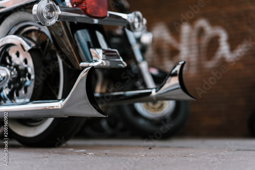 Shiny chromed retro fishtail exhausted pipes of luxury motorcycle. Brick wall with defocused graffiti in background. Soft lighting, vintage look