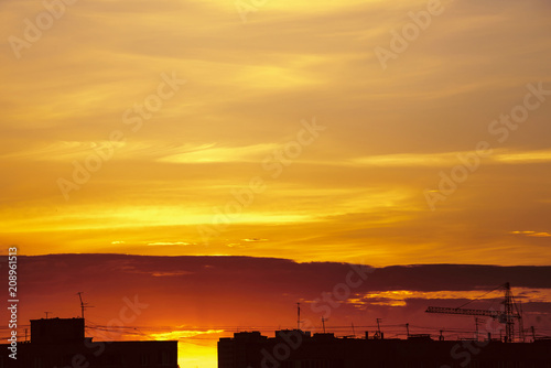 Beautiful cloudy dramatic morning sky above silhouette of city buildings. Picturesque dawn in city. Background of varicolored clouds. Unimaginable fantasy sunrise in heaven. Silhouette of tower crane. © Daniil