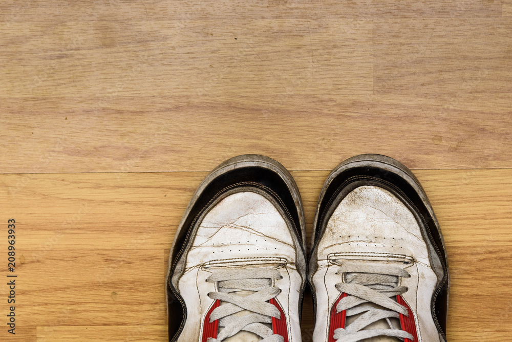 A pair of dirty used sneakers isolated on a laminated wooden floor A pair of dirty used sneakers isolated on a laminated wooden floor