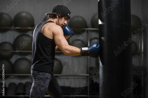Muscular young boxer training with punching bag