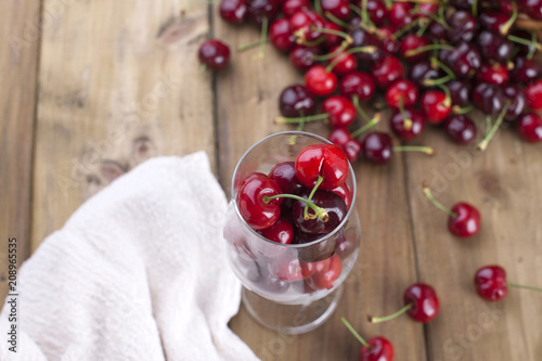 A large basket of ripe cherries and scattered berries on a table and in a glass. Wooden background, free space for text. Retro style. Copy space