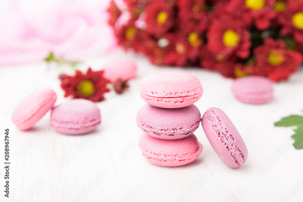 Obraz premium Set of french macaroons on wooden table. Sweet pink and violet macaron cakes and a red chrysanthemum flowers. 