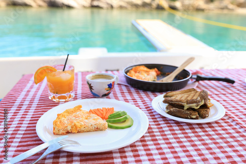 A simple breakfast of omelet, pieces of avocado and carrots, toast with cheese, a cup of coffee and a glass of fresh orange juice during a summer holiday on a yacht.