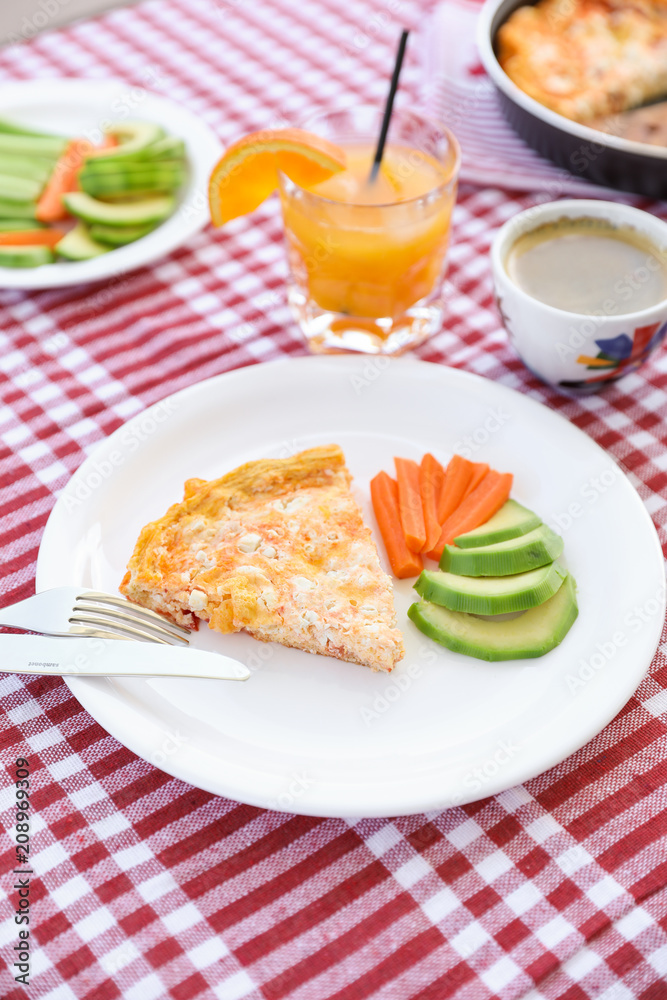 A simple breakfast of omelet, pieces of avocado and carrots, a cup of coffee and a glass of fresh orange juice during a summer holiday on a yacht.
