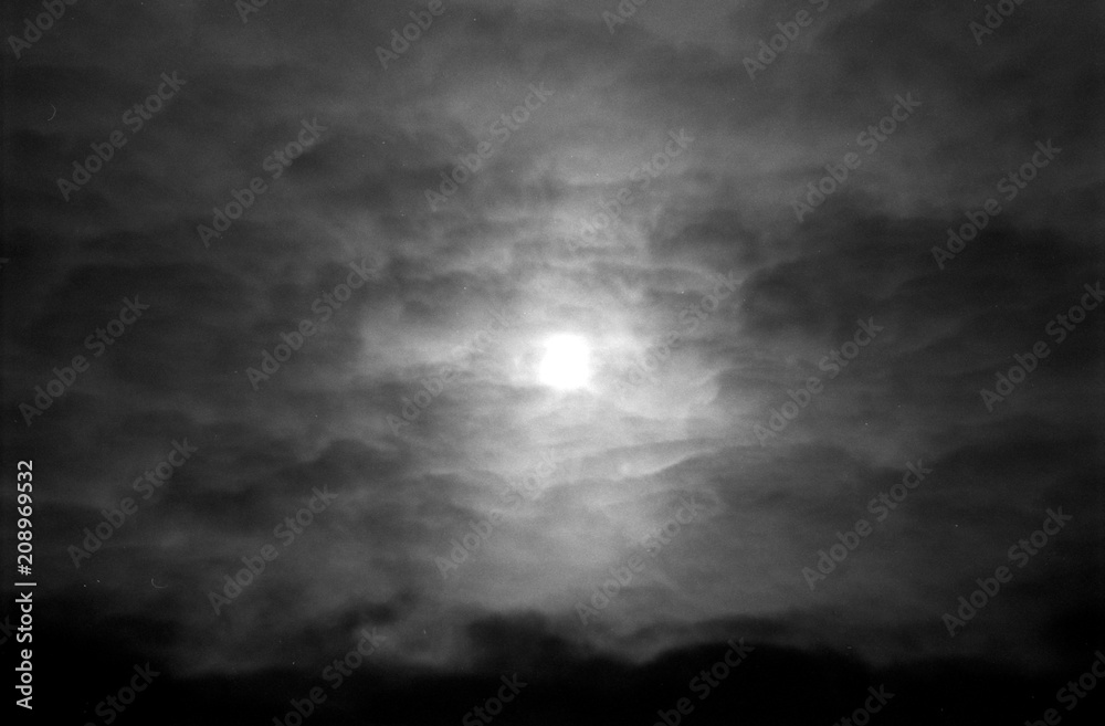 Dramatic cloudy sky in grayscale on film. Overcast weather and sun through cumulus clouds. Monochrome atmospheric dark scanned analog photography with grain and scratch. Lomography of nature.