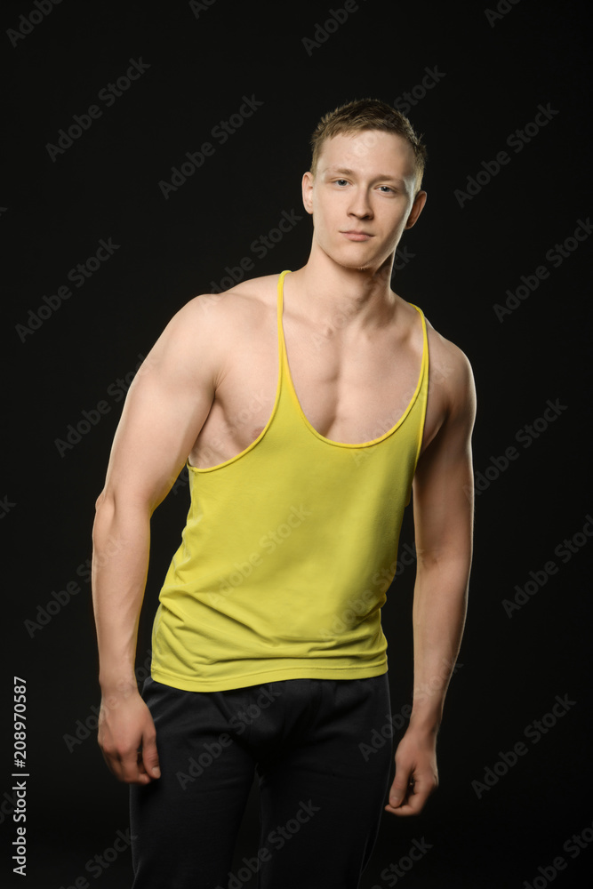 a young bodybuilder in a t-shirt posing on a black background and looking at the camera