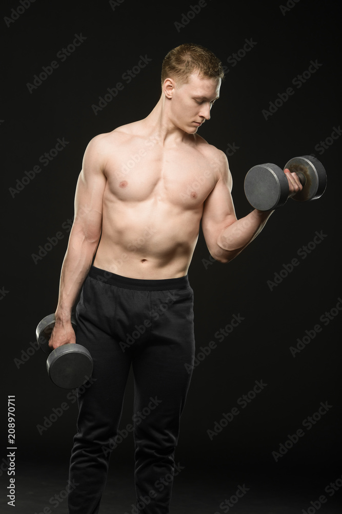young bodybuilder raises dumbbells on black background