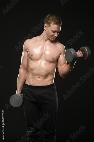 a guy with a beautiful body trains with dumbbells on a black background © Vladimir
