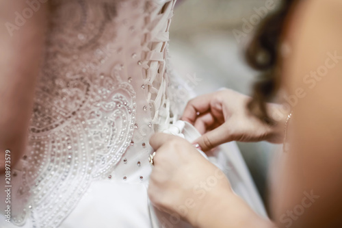 Wedding. Bridesmaid preparing bride for the wedding day. Bridesmaid helps fasten a wedding dress the bride before the ceremony. Luxury bridal dress. selective focus photo