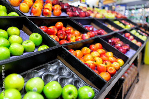 Many varieties assorted red apples on display shelf in grocery store boxes in aisle, supermarket inside, nobody, including granny smith green