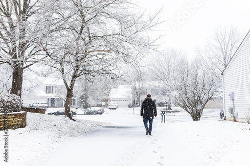 Man walking in driveway in neighborhood with snow covered ground during blizzard white storm, snowflakes falling in Virginia suburbs, single family homes to check mail in mailbox photo