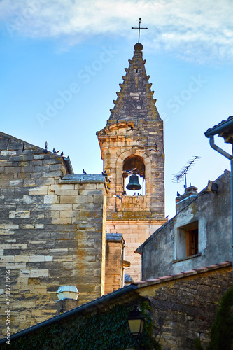 View of the church tower with a bell and a cross and roofs of houses with sitting pigeons