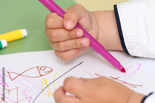close up on the hand of a child who draws with colored markers
