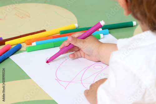 close up on the hand of a child who draws with colored markers
