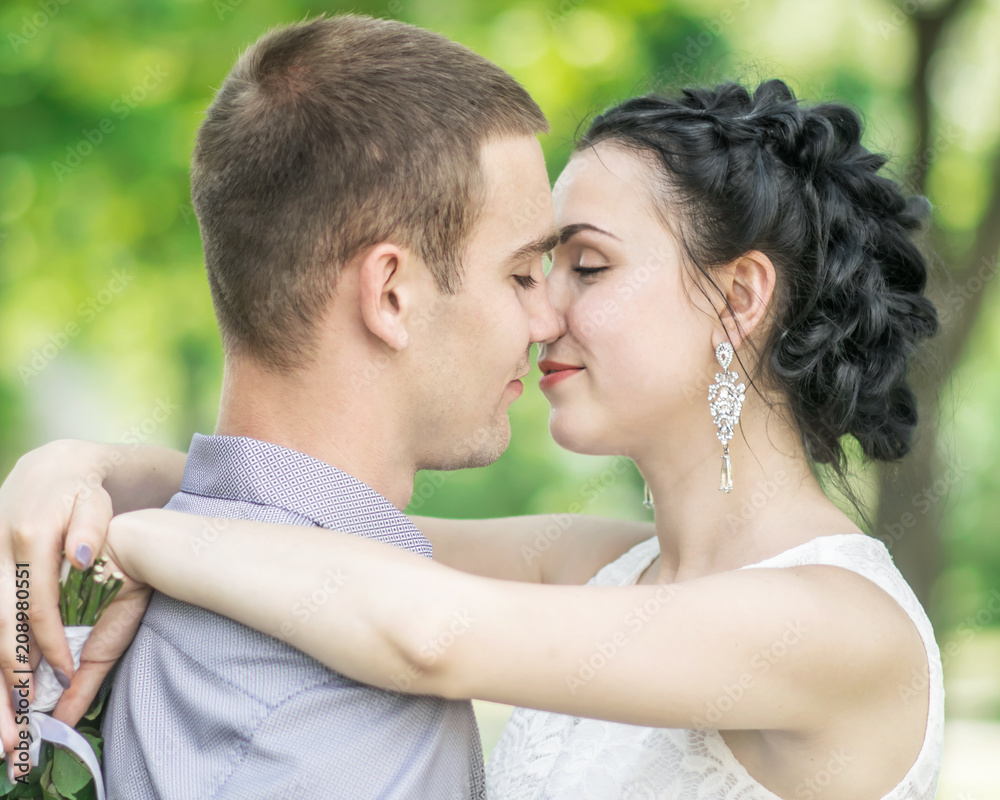 Close-up portrait of beautiful young couple female bride and male bridegroom kissing in summer park. Woman wife hugging man husband