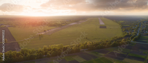 Aerial view from the drone, a bird's eye view of abstract geometric forms of abandoned runway, forests and agricultural fields in the summer evening at sunset.