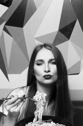 Portrait of attractive long haired woman with slightly ajar mouth and red lips eating Italian pasta with seafood and vegetables. Gorgeous young female model posing with delicious fettuccine on fork. photo