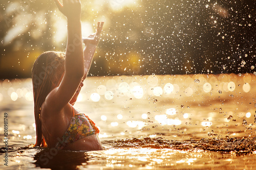 little girl playing in the river. A girl with blond hair raises her hands up in the water and splashes water drops