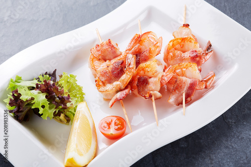Grilled shrimps. Shrimps skewers, lemon and fresh herbs and tomatoes on plate.