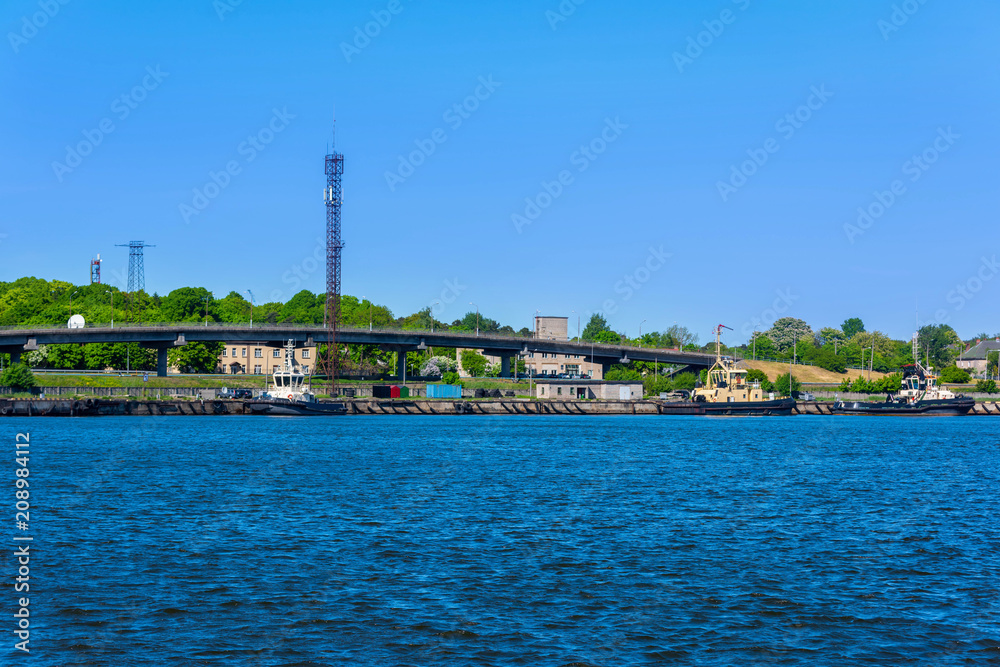 A quiet harbor on a sunny day, clear sky, beautiful green trees, ships and a bridge