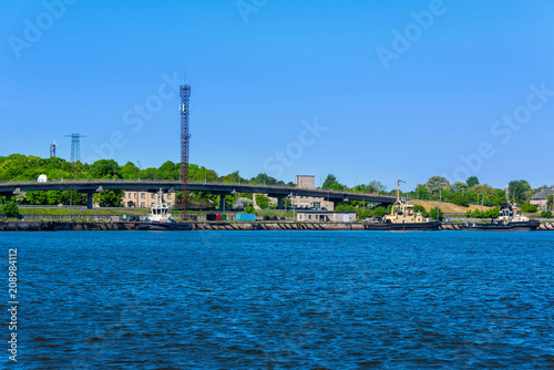 A quiet harbor on a sunny day, clear sky, beautiful green trees, ships and a bridge