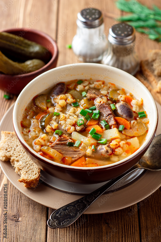 Traditional Russian soup Rassolnik with pickled cucumbers and pearl barley in bowl on wooden table Traditional Russian soup Rassolnik with pickled cucumbers and pearl barley in bowl on wooden table