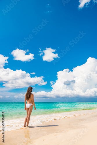 Beach vacation travel luxury swimsuit woman relaxing on summer holidays with copy space ocean, white sand and blue sky paradise landscape background.