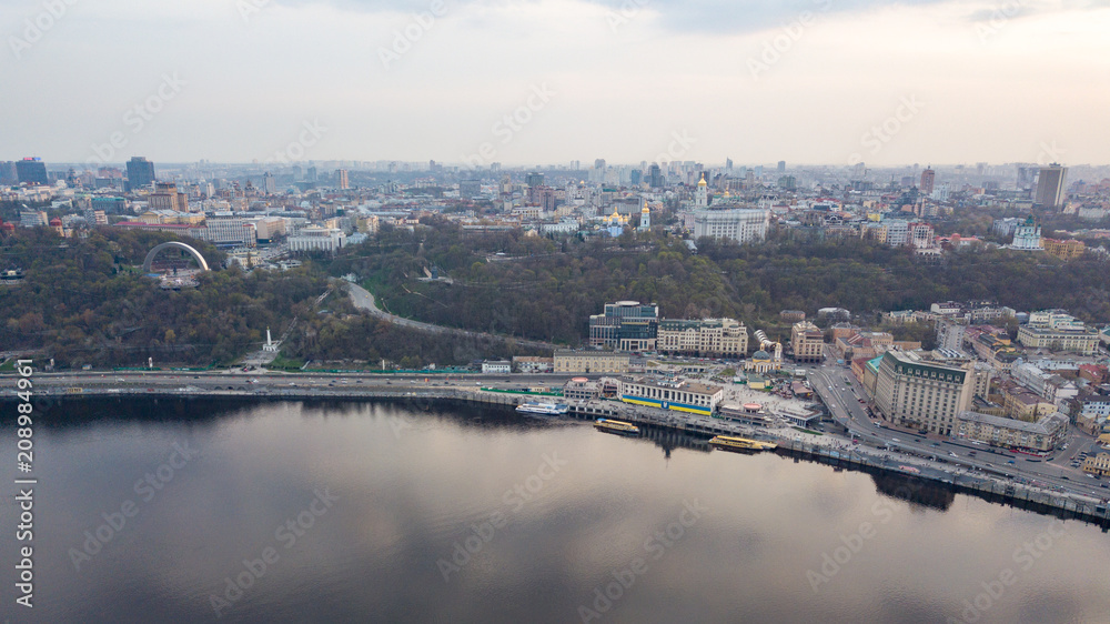 The panoramic bird's eye view shooting from drone of the Podol district, the right bank of the Dnieper River and centre of Kiev, Ukraine at summer sunset on the background of the cloudy sky.