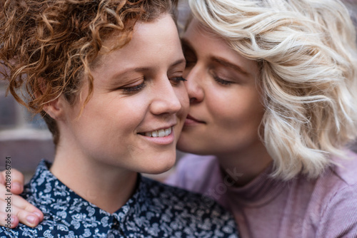 Young woman giving her smiling girlfriend an affectionate kiss 