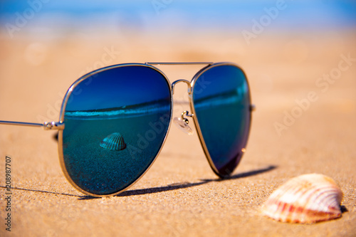Stormy sea and shell are reflected in the mirror sunglasses on tropical beach