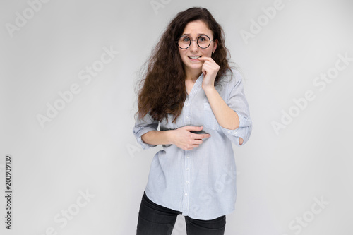 Portrait of a young girl in glasses. Beautiful young girl on a gray background. The girl is gnawing at the nail. photo