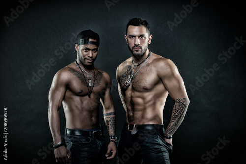Machos with muscular tattooed torsos look attractive, dark background. Guys sportsmen with sexy muscular torsos. Masculinity concept. Athletes on confident faces with nude muscular chests