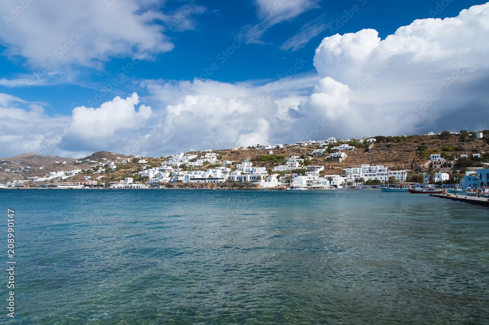Sea village or town on mountain landscape with nice architecture in Mykonos, Greece. Houses at sea coast on cloudy blue sky. Summer vacation on mediterranean island. Wanderlust and travelling concept